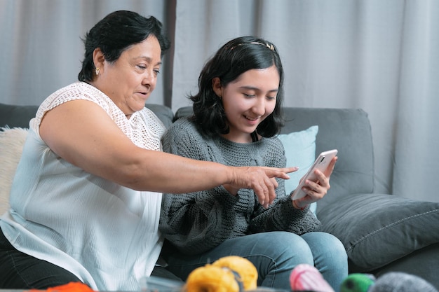 Older woman 60 year old latin grandmother using cell phone and having fun with her granddaughter