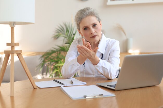 Older woman doctor therapist wearing headset video call talking to web camera consulting virtual patient online by video conference call chat.