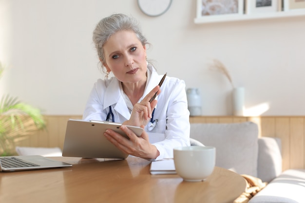 Older woman doctor therapist wearing headset video call talking
to web camera consulting virtual patient online by video conference
call chat.