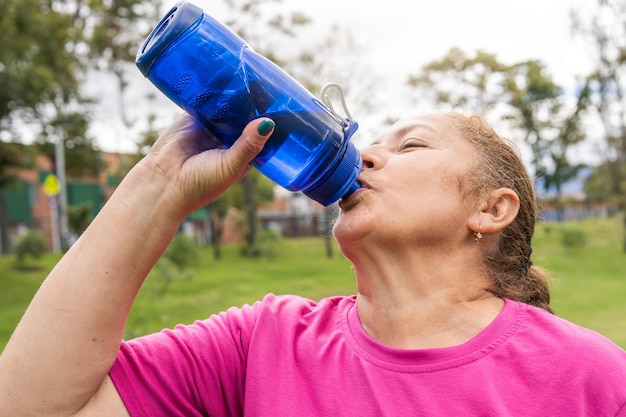 Older woman drinking water after exercising in the park