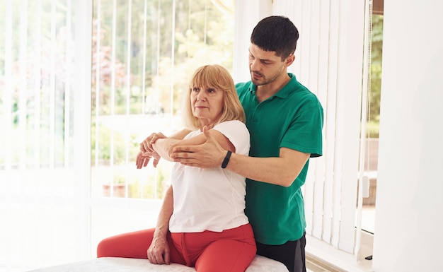 Older woman have a visit in clinic and having rehabilitation Male instructor helping her