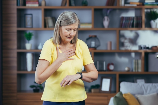 La donna anziana a casa che fa fitness ha una grave mancanza di respiro e dolore al petto confronta i proiettili sui braccialetti per il fitness