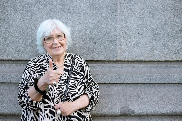 Older woman looking into camera with thumbs outdoors