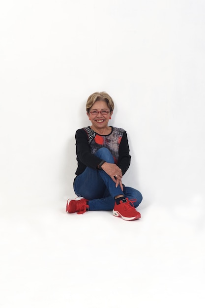 Older woman sits on the floor and leans against a wall on white background