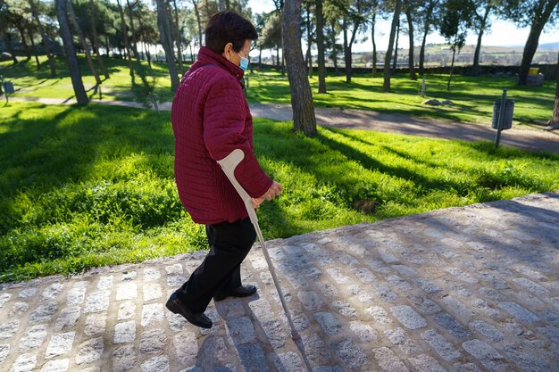 Donna anziana che cammina nel parco cittadino con maschera e distanza sociale a causa del coronavirus. spagna.