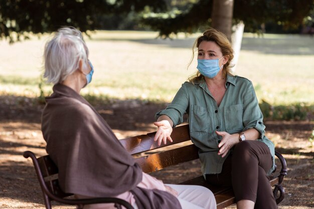 Older woman with medical mask conversing outdoors on bench