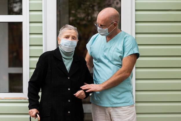 Foto donna anziana con mascherina medica aiutata dal suo infermiere