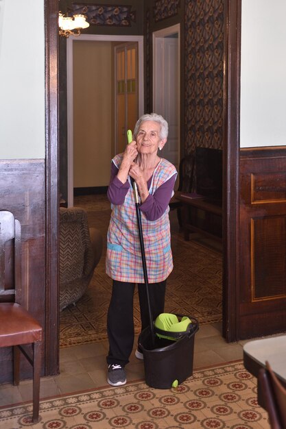 Donna anziana con la scopa che fa il pavimento della sua casa