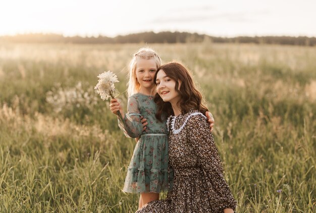 Older and younger sisters walk together in nature in the summer. sister hugs and soothes