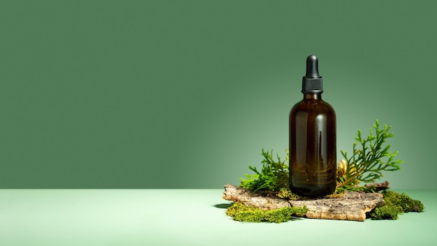 Olie met serum voor huid- en haarverzorging Een concept van etherische oliemos en boomschors op een groene achtergrond Glazen bruine fles lichaamsolie met een druppelaar Zelfzorg en wellness Copy space Banner