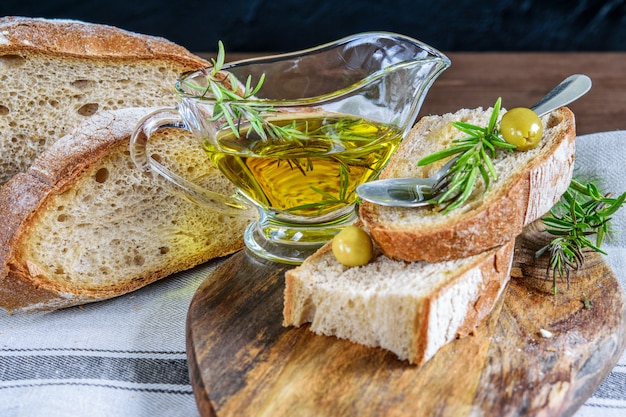 Olijfolie in de transparante glazen kom op de houten snijplank. gesneden integraal brood, olijven en rozemarijn. gezond mediterraan eten concept.