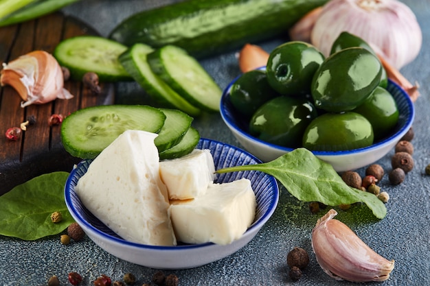 Olijven, kaas, knoflook, peperbollen en groene uien op een blauwe en houten standaard. Gezond eten