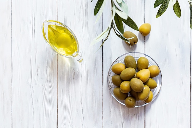 Olio d'oliva e ciotola di olive verdi su un tavolo di legno bianco