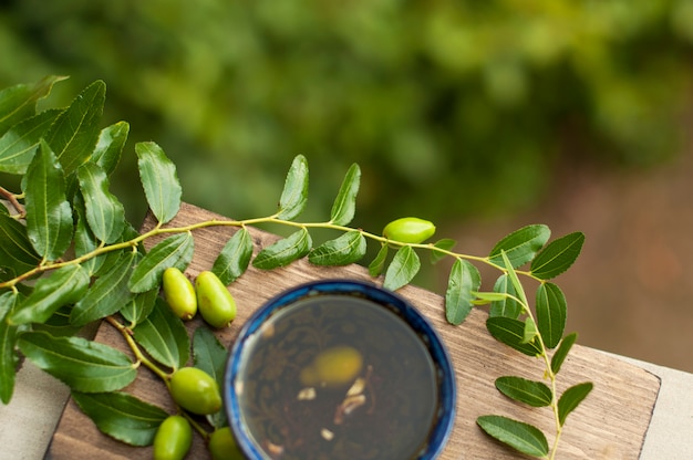 the olive oil in the cup. Branch of an olive tree with fresh olives. Green olives. In the garden. On a wooden board. a jug for oil. Italian classics. Olives of Italy. Food of Italy