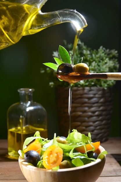 Foto olio d'oliva che cade su due olive con foglie di ulivo per insaporire un'insalata mediterranea.