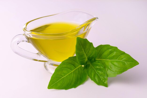 Olive oil in a glass gravy boat and a sprig of basil on a white background Closeup