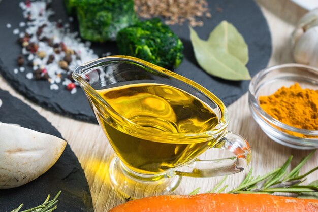 Olive oil in a glass gravy boat on the table with food ingredients, food background