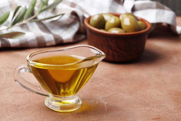 Olive oil in a gravy boat and an olive branch on the table.