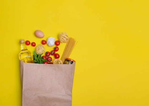 Foto olio d'oliva, pasta, tagliatelle, olive, uovo, pomodorini, aglio in un sacchetto di carta sul giallo