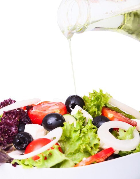 olive oil pouring into bowl of salad isolated on white