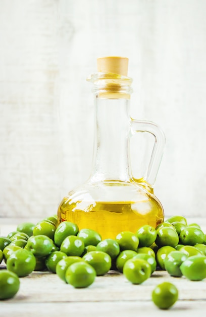 The olive oil in a transparent bottle on a wooden background. Selective focus.