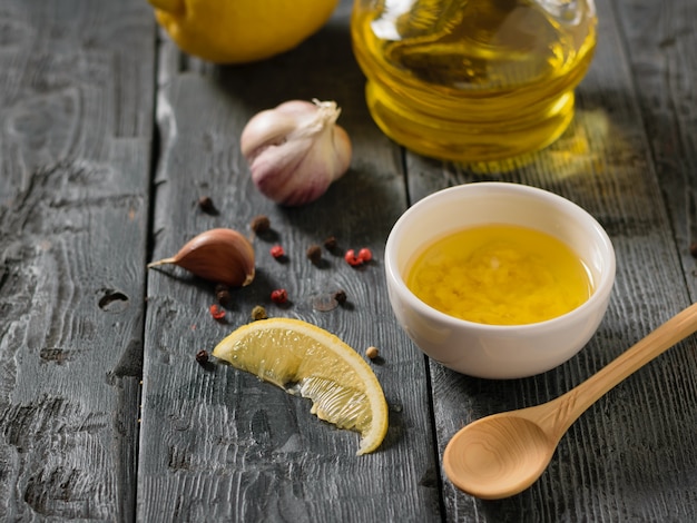 Olive oil with garlic and lemon in a white bowl on a wooden table. Dressing for diet salad.