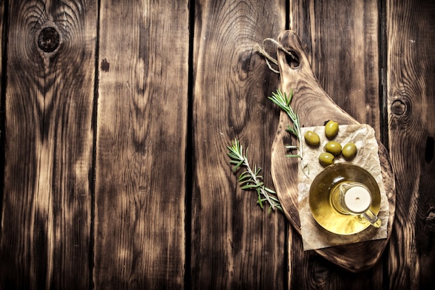 Olive oil with rosemary branch. On wooden background.