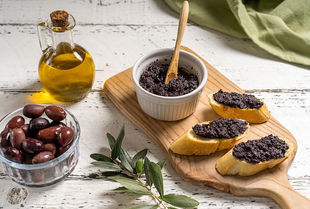 Patè di olive in una ciotola e spalmato su fette di pane sul tagliere di legno