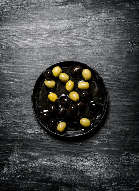 Photo olives and black olives in an old pan on black rustic background