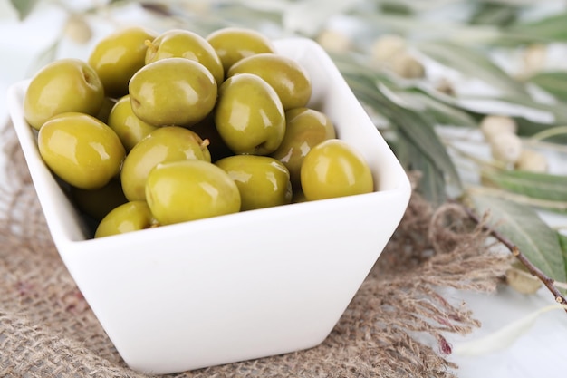 Olives in bowl with branch on sackcloth close up