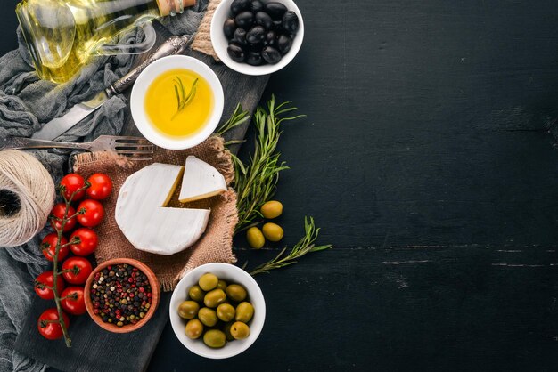 Foto olive olio d'oliva formaggio e spezie su uno sfondo di legno nero spazio libero per il testo