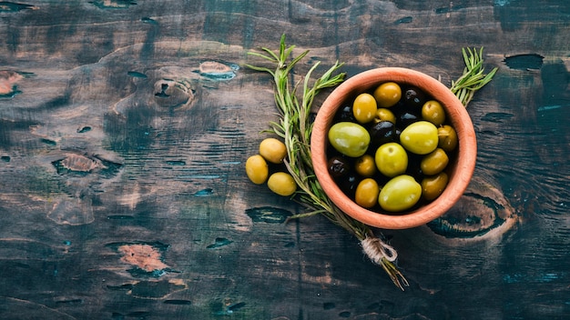 Foto olive in un piatto e rosmarino su uno sfondo di legno nero spazio libero per il testo