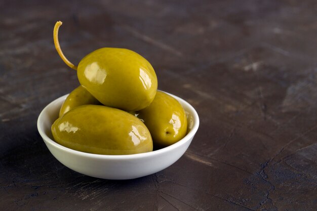 Olives in white bowl on dark background.