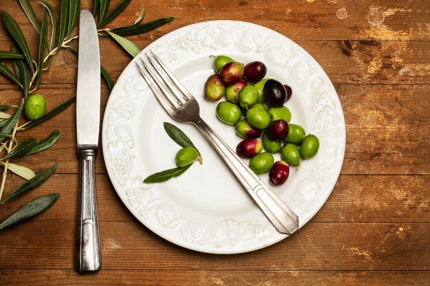 Olives on a white plate on a wooden table in a top view