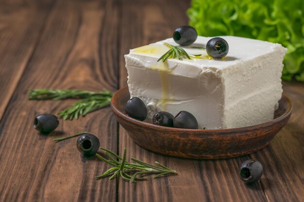 Olive con un grosso pezzo di feta su un tavolo di legno. insalata con formaggio e verdure.