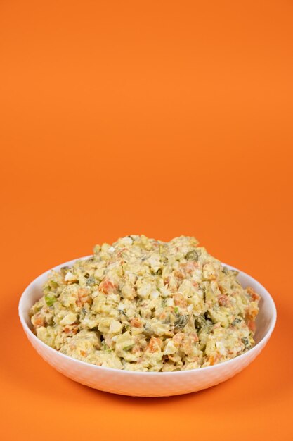 Olivier russian salad in a plate on an orange background closeup