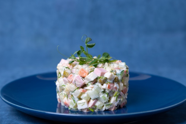 Olivier salad on a blue plate, decorated with pea sprouts. Traditional New Year and Christmas Russian salad. Close-up, selective focus, blue background.