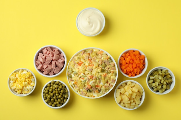 Olivier salad and ingredients on yellow background