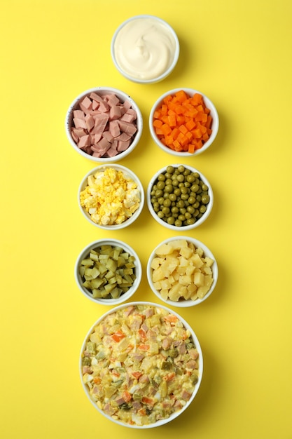 Olivier salad and ingredients on yellow background