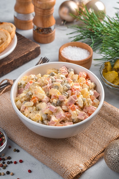 Olivier salad in a white bowl on a Christmas background. Side view, vertical.