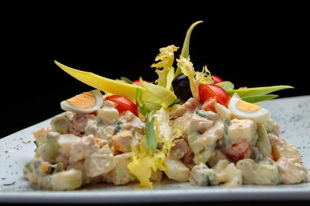 Olivier salad on a white plate on a dark background