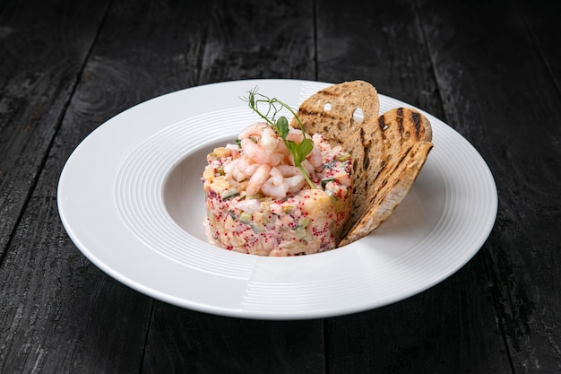 Insalata olivier con frutti di mare e caviale su un tavolo scuro