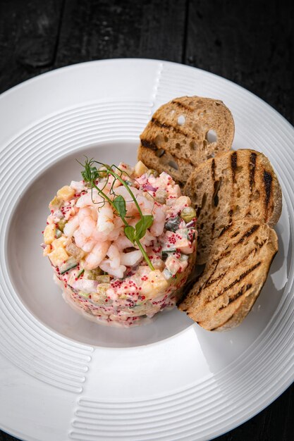 Olivier salad with seafood and caviar on a dark table