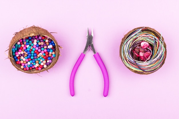 Ð¡olored beads in halves of coconut, cords, shell beads and pliers on pink background
