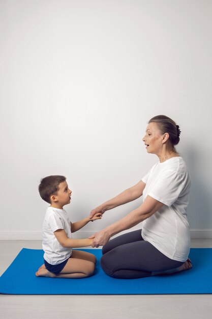 Oma en haar kleinzoon zitten thuis op een yogamat in een wit appartement