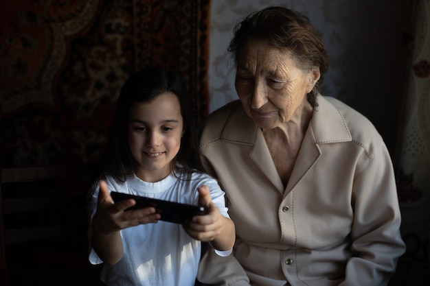 Oma en kleindochter. Een schattig klein meisje laat haar grootmoeder een smartphone zien.