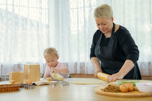 Oma en kleindochter rollen deeg op houten tafel bestrooid met bloem. familietradities concept. Saamhorigheid Concept. Zelfgemaakte bakles concept. bloggen concept