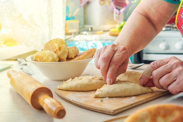 Oma kookt taarten. Thuis gekookt voedsel. Omemade taarten van het deeg in de handen van de vrouwen. Het proces van het met de hand maken van taartdeeg