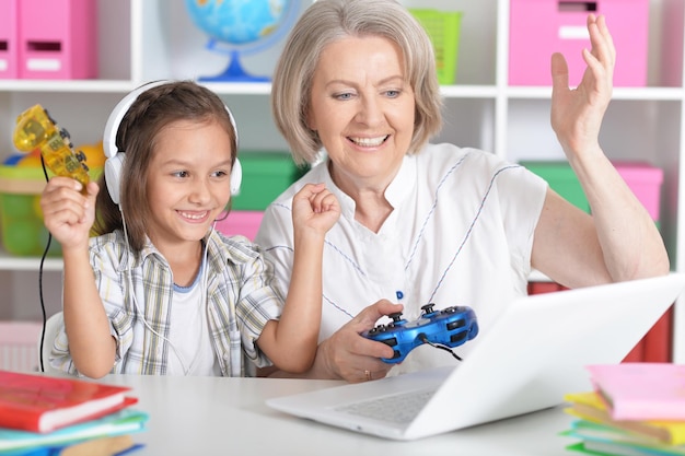 Oma met haar kleindochter die thuis computerspel speelt op laptop