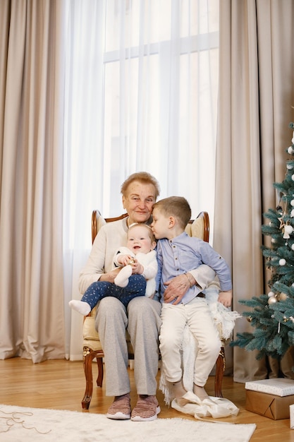 Oma met haar kleindochter en kleinzoon zitten bij de kerstboom